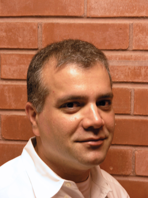 A head-and-shoulders photo shows a man looking at the camera with a small smile, with a brick wall in the background